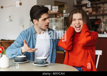 Déçu couple homme et femme 20s de crier et d'avoir à redire tout en ayant pause café dans cafe Banque D'Images