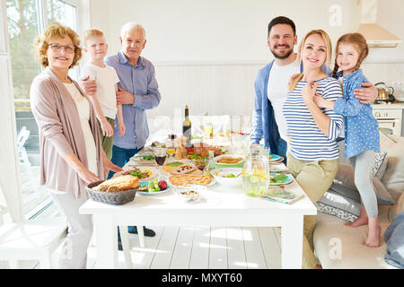 Portrait of two generation family de dîner ensemble posant round table de fête avec des plats délicieux et smiling at camera dans sun moderne Banque D'Images