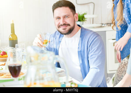 Portrait of smiling young man looking at camera et tenant un verre de vin tout en profitant d'un dîner de famille à la lumière du soleil, copy space Banque D'Images