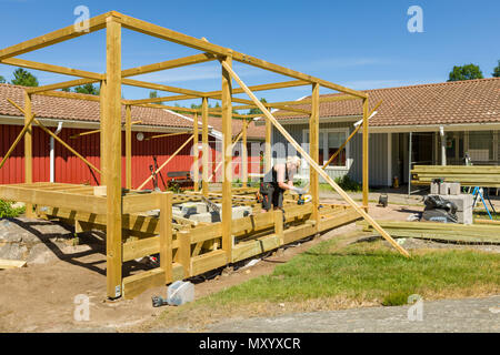 Menuisiers travailler à l'extérieur sur l'érection d'une grande terrasse avec pergola et un foyer rond Banque D'Images