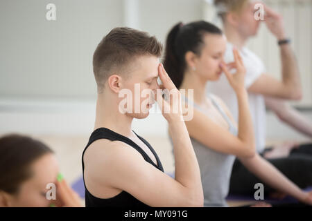 Groupe de jeunes sportifs pratiquant le yoga leçon, faire un exercice de respiration, l'autre narine, le pranayama nadi sodhana, travaillant hors piscine close up, Banque D'Images