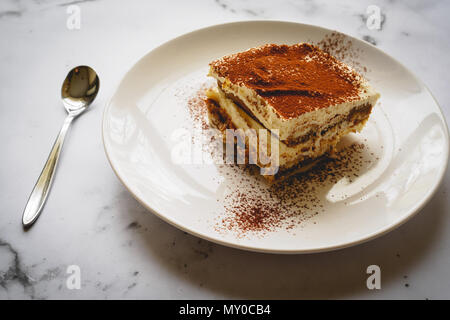 Gros plan d'une tranche de tiramisu traditionnel fait maison (dessert italien) sur une plaque blanche avec une cuillère sur un en conseil. Le format paysage. Banque D'Images