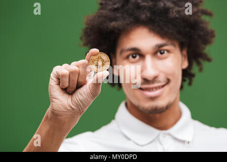 Image of young African man bouclés isolated over Green wall background bitcoin holding. Banque D'Images