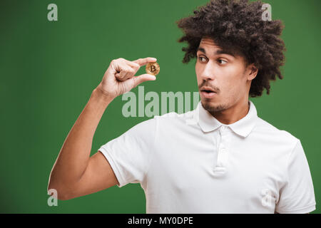 Image of young African man isolated bouclés sur green wall background bitcoin holding. Banque D'Images