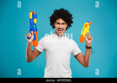 Portrait d'un jeune excité african man holding deux pistolets à eau isolé sur fond bleu Banque D'Images