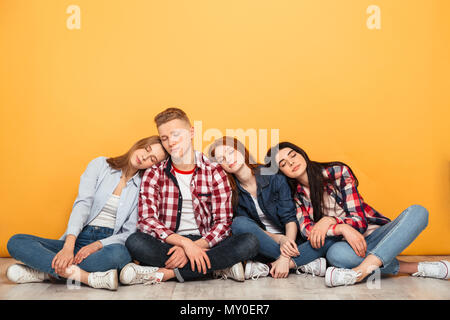 Groupe de jeunes amis de l'école s'ennuyer assis sur un étage et une chambre sur fond jaune Banque D'Images