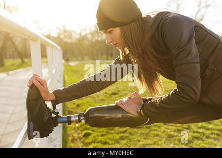 Droit des personnes handicapées en faisant courir femme sportswear pentes et stretching prothèse sur l'herbe à l'aide de garde-fous Banque D'Images