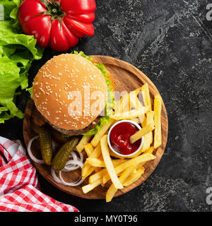 Hamburger, frites, les cornichons et le ketchup sur planche de bois. Le fast food. Burger fait maison et de pommes de terre frites. Vue supérieure avec copie espace pour le texte Banque D'Images