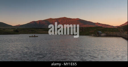 Les palettes pêcheur solitaire sur son bateau afin de Snowdon à travers Llyn Y Dywarchen, Gwynedd, Pays de Galles, Royaume-Uni Banque D'Images