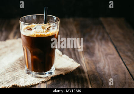 Café glacé noir dans un grand verre avec une paille sur une table en bois rustique Banque D'Images