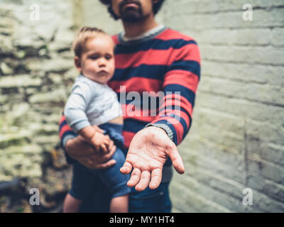 Un jeune homme avec des taches sur les mains de maladie est mendier avec un bébé à l'extérieur Banque D'Images