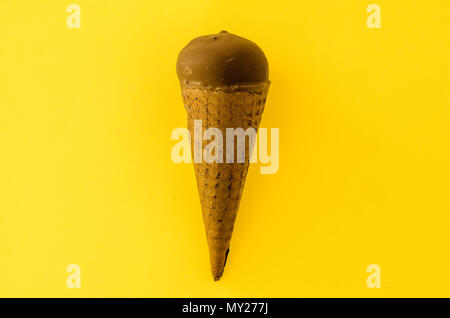 Crème glacée à la vanille avec de la confiture de canneberges dans un cône de sucre trempé dans du chocolat sur fond jaune.couleur pastel.rafraîchir en été.Copie d'espace Banque D'Images