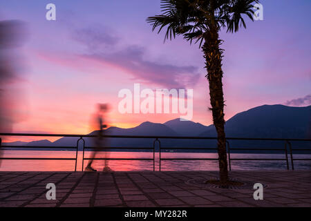 Beau coucher de soleil brumeux sur le lac d'Iseo, Lombardie, Italie. Silhouettes de personnes marchant sur la rue de la promenade en ville d'Iseo. Célèbre station Italienne Banque D'Images