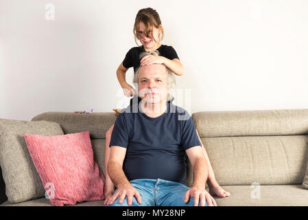 Petite Fille peignant et faire des tresses ou des nattes à son père sur le canapé à la maison Banque D'Images