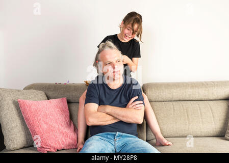 Petite Fille peignant et faire des tresses ou des nattes avec des oursons gélifiés et les liens de son père avec une patience face sur le canapé à la maison Banque D'Images