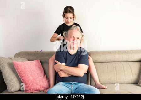 Petite Fille peignant et en faisant des tresses ou nattes avec différentes couleurs de gummies et ses liens avec son père sur le canapé à la maison Banque D'Images