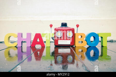 Le mot CHAT BOT avec une tête de robot rouge sur un sol en bois avec réflexion Banque D'Images