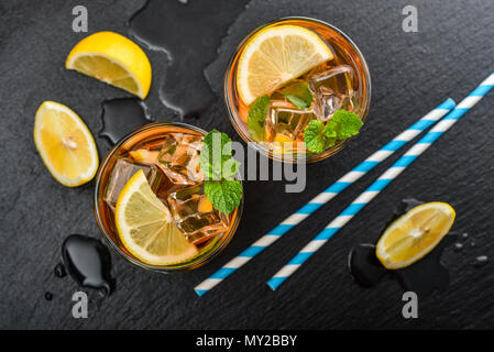 Deux verres de thé sucré glacé au citron et à la menthe et des pailles en papier rétro sur fond d'ardoise noire, vue du dessus Banque D'Images