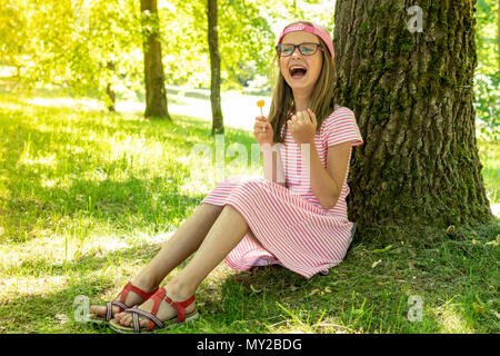 Laughing girl lollipop,tenir assis sous tree in park Banque D'Images