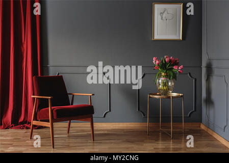 Salle d'attente simple intérieur avec un seul fauteuil rouge debout contre un mur gris foncé au moulage à côté d'une table d'or avec des fleurs roses. Du vrai ph Banque D'Images