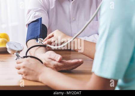Libre de main du patient et un médecin mesurer sa pression artérielle sur un bureau en bois Banque D'Images