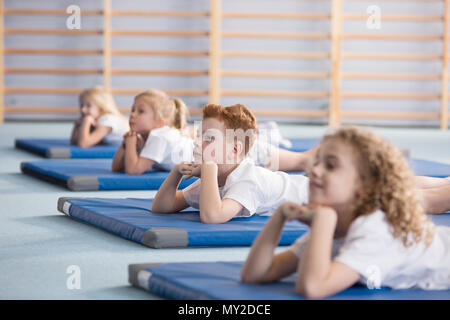 Garçon sur un tapis bleu relaxant avec des amis dans une école primaire Banque D'Images