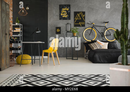 Affiches noir et jaune sur le mur de béton à l'intérieur spacieux avec un vélo derrière un lit noir et jaune avec l'espace d'étude président et bureau. Du vrai ph Banque D'Images
