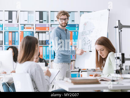 Réunion des étudiants en génie et discuter des idées dans le laboratoire, un étudiant est écrit sur un tableau. Banque D'Images