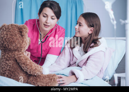 Médecin jouant avec un stéthoscope, examinant une peluche et a sick girl smiling Banque D'Images
