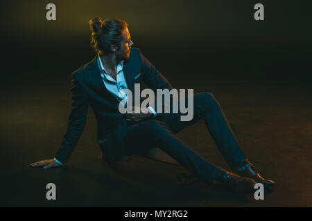 Jeune homme élégant en costume élégant assis sur planche Banque D'Images