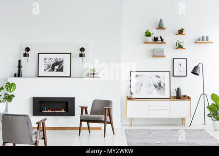 Fauteuils gris en blanc grand salon intérieur avec des affiches et cheminée. Photo réelle Banque D'Images