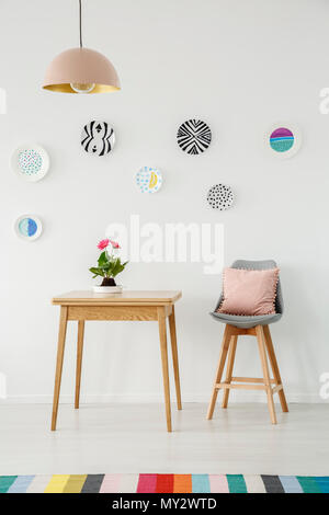 Fleurs roses sur la table à côté d'une chaise contre le mur gris blanc avec des plaques à motifs colorés à l'intérieur de salle à manger Banque D'Images