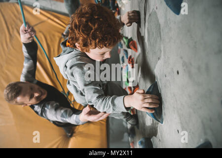 Petit garçon dans un harnais escalade un mur à gym avec son père lui de fixation de l'arrière Banque D'Images