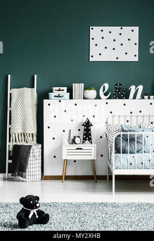 Ours noir jouet sur un tapis vert foncé dans une chambre pour un enfant d'un mobilier blanc et motif à pois Banque D'Images