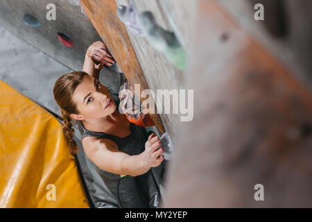 Un grand angle shot de jeune femme dans une tenue sportive escalade un mur avec prises at gym Banque D'Images