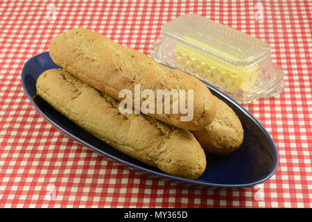 Miches de pain de blé entier pour sandwichs sous-marin sur plateau bleu avec du beurre dans du verre beurrier Banque D'Images