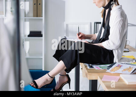 Cropped shot de créateur de mode de dessin dans l'album tout en étant assis sur un bureau Banque D'Images