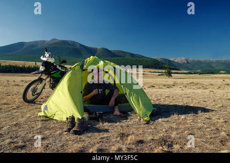 Homme assis au camp tente avec moto enduro voyageur seul steppe paysage en arrière-plan de hautes montagnes au coucher du soleil Montagnes de l'Altaï en Sibérie Banque D'Images