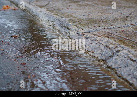 Dans un jour de pluie, l'eau coule le long du trottoir. Focalisation étroite. Banque D'Images