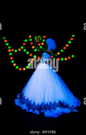 Séance photo de mariage de la mariée avec des fleurs de couleurs vives photographie néon sur fond sombre dans les rayons ultraviolets jeune fille en robe de mariée blanche de style vogue posant dans Banque D'Images