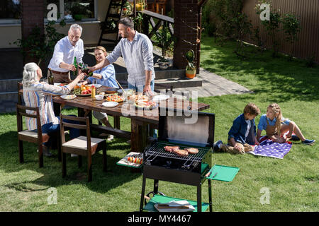 Adultes clinking glasses avec boissons pendant que les enfants se reposant sur drapeau américain au cours de barbecue familial Banque D'Images