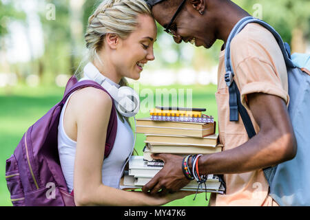 Vue latérale d'happy young couple holding books ensemble multiethnique tout en se tenant dans park Banque D'Images