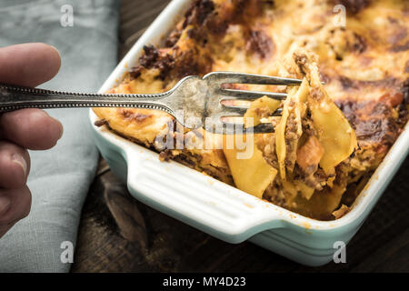 Manger de la lasagne italienne avec la fourchette sur fond de bois foncé Banque D'Images