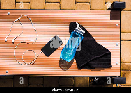 Vue de dessus du smartphone avec écouteurs, bouteille d'eau et serviette sur banc en bois Banque D'Images