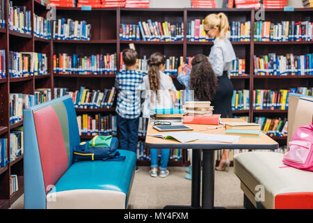 Jeune enseignant d'apprentissage avec les enfants dans la bibliothèque Banque D'Images