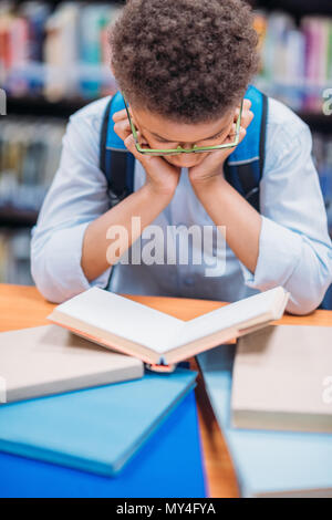 Écolier américain africain concentré reading book in library Banque D'Images