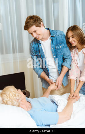 Smiling Young couple holding hands of an elderly woman lying in hospital bed Banque D'Images