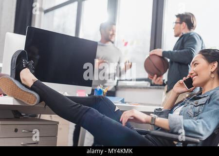 Femme parlant sur smartphone en face d'hommes avec ball at office Banque D'Images