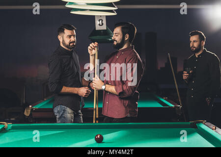 Smiling man frotter avec de la craie blanche à côté d'une table de billard au bar avec des amis Banque D'Images