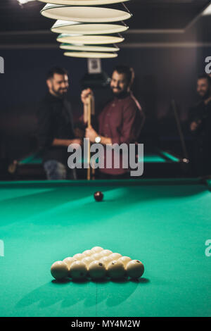 Smiling man frotter avec de la craie blanche à côté d'une table de billard au bar avec des amis Banque D'Images